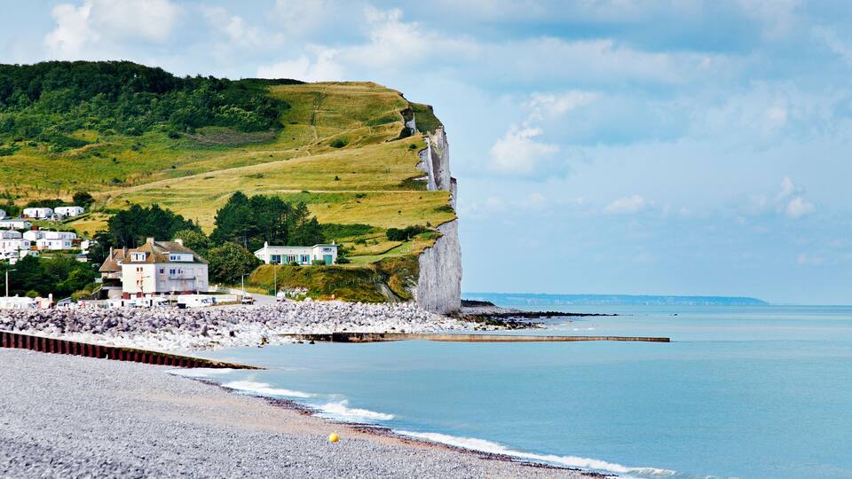 A coastal town with white houses on a hillside, a rocky beach, and a cliff.