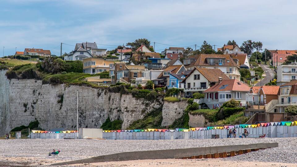 A coastal town with houses on a cliff, a beach, and colorful flags.