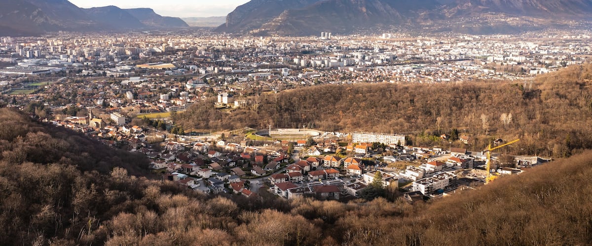 A city with a mountainous backdrop, featuring a mix of residential and commercial buildings, a stadium, and a construction site.