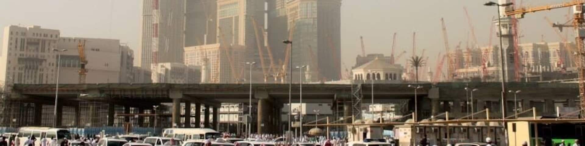 A hazy look at the Makkah Clock Tower, tallest & largest clock tower in the world (601 meters), under the Arabian sun.
The clock tower stands in the center of a high-rise complex called Abraj Al-Bait. Six smaller high-rises surround it at heights varying and accommodate both residential and hotel uses. True to its name, four colossal clock faces are mounted near the top of the tower. These clocks hold the record for both the largest and highest in the world. At night, the clock faces are illuminated by one million LED lights that transform the tower into a green and white beacon. Writing is inscribed above each clock, with the words “God is the Greatest” on the north and south sides, while the Koran adorns the east and west sides. The spire of the tower features a spherical observation center at its base. The spire is capped with a shining mosaic gold crescent that weighs 35 metric tons. A number of cultural amenities are present in the upper levels of the tower, including a center for lunar observation and a cosmology museum.