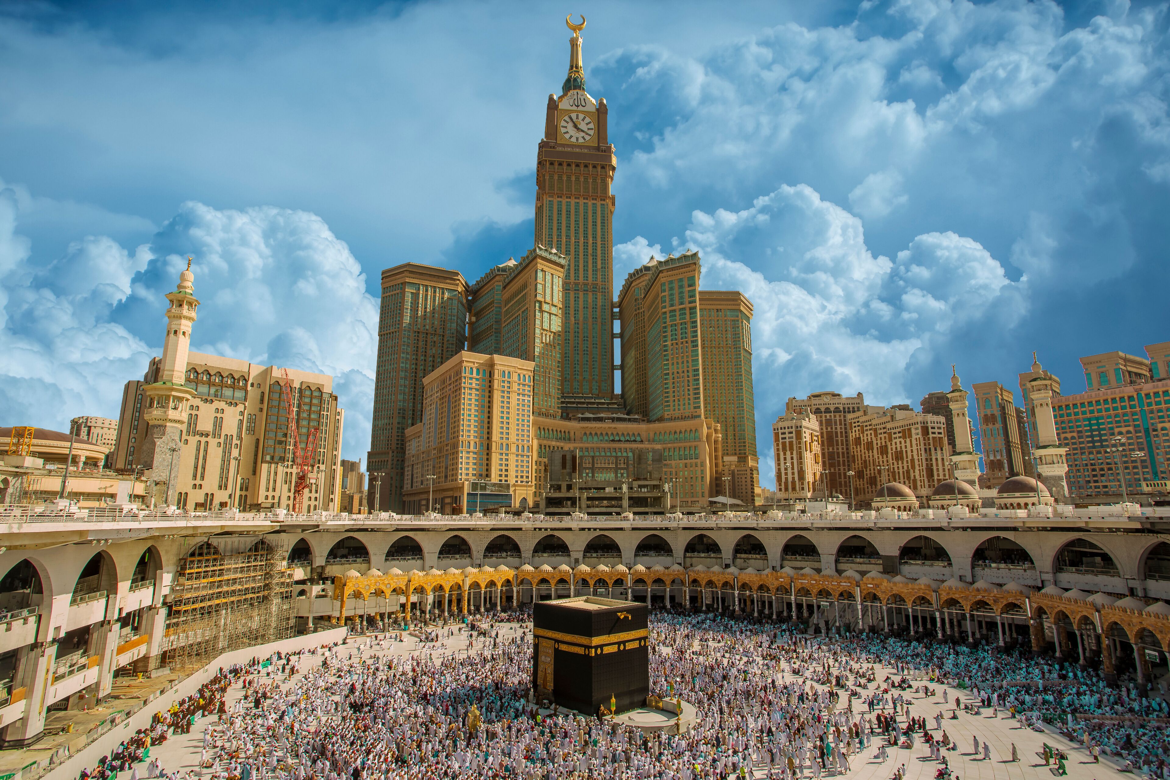 A large mosque with a minaret and a clock tower, surrounded by a crowd of people.