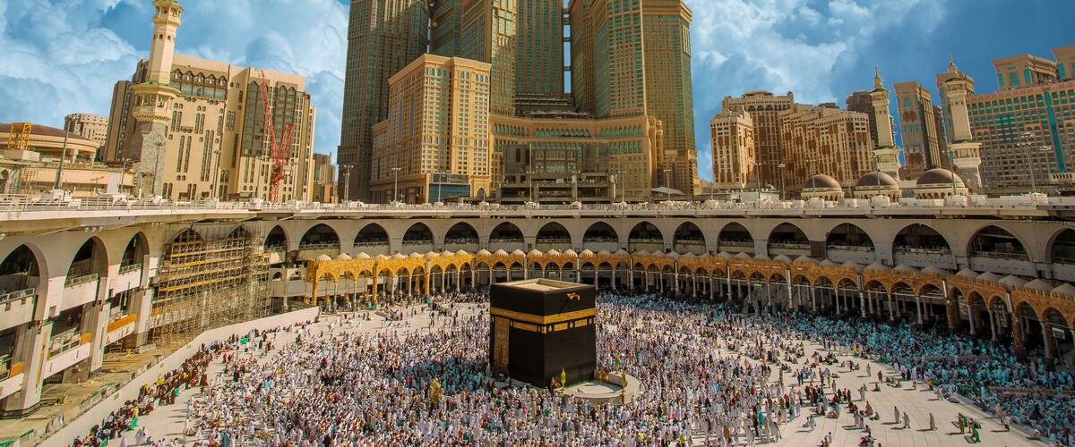 A large mosque with a minaret and a clock tower, surrounded by a crowd of people.