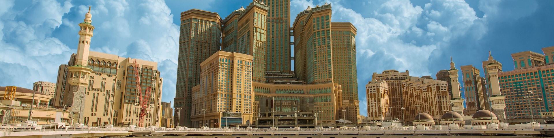 A large mosque with a minaret and a clock tower, surrounded by a crowd of people.