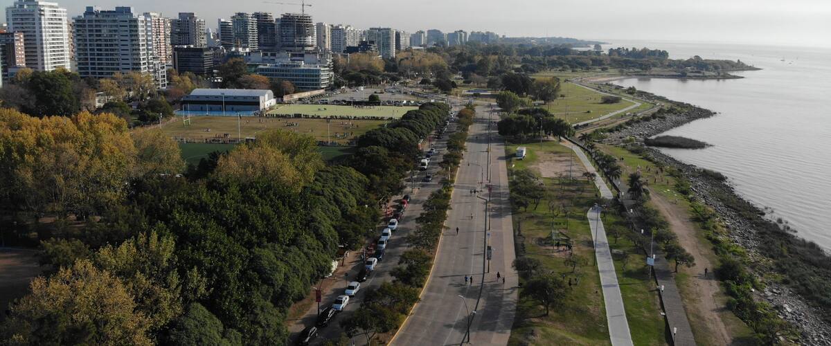 An aerial view of a coastal city with high-rise buildings, a park, and a waterfront promenade.