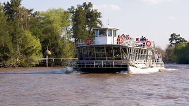 A riverboat with passengers, surrounded by trees and a calm water surface.
