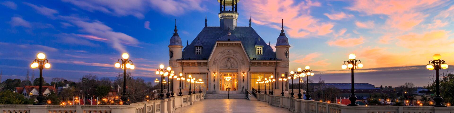 A grand building with a dome and multiple towers, surrounded by a well-lit pathway and ornate street lamps.