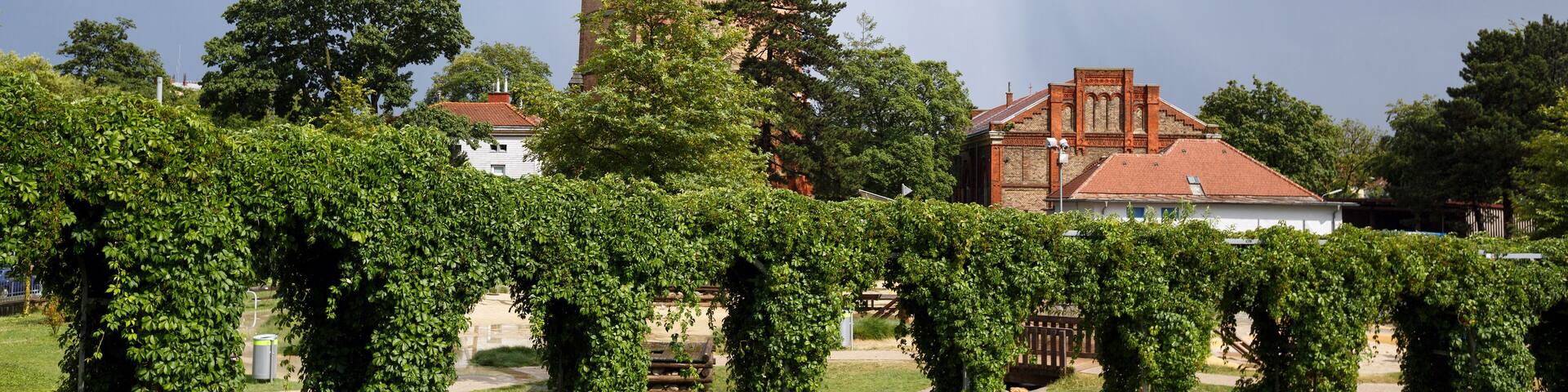 A historic tower with a dome and spire, surrounded by a well-maintained garden with ivy-covered arches.