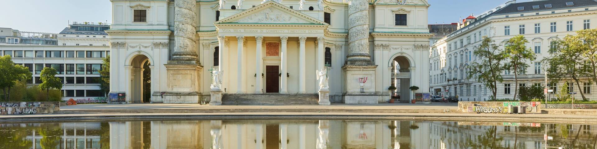 A historic church with a large dome and twin towers, reflected in a calm body of water.