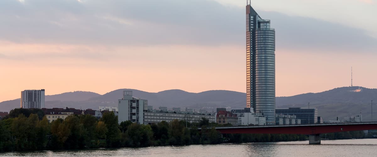 A modern skyscraper with a unique design, a river, and a bridge in the foreground.