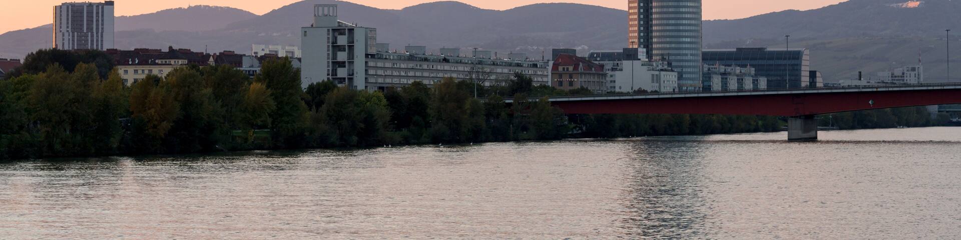 A modern skyscraper with a unique design, a river, and a bridge in the foreground.
