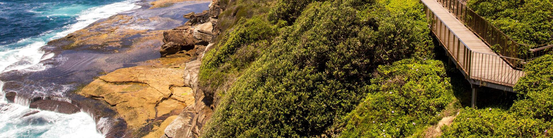 A coastal landscape with a wooden boardwalk, rocky cliffs, and a cemetery with headstones.