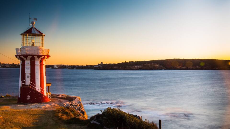 A red and white lighthouse by a calm sea at sunset.