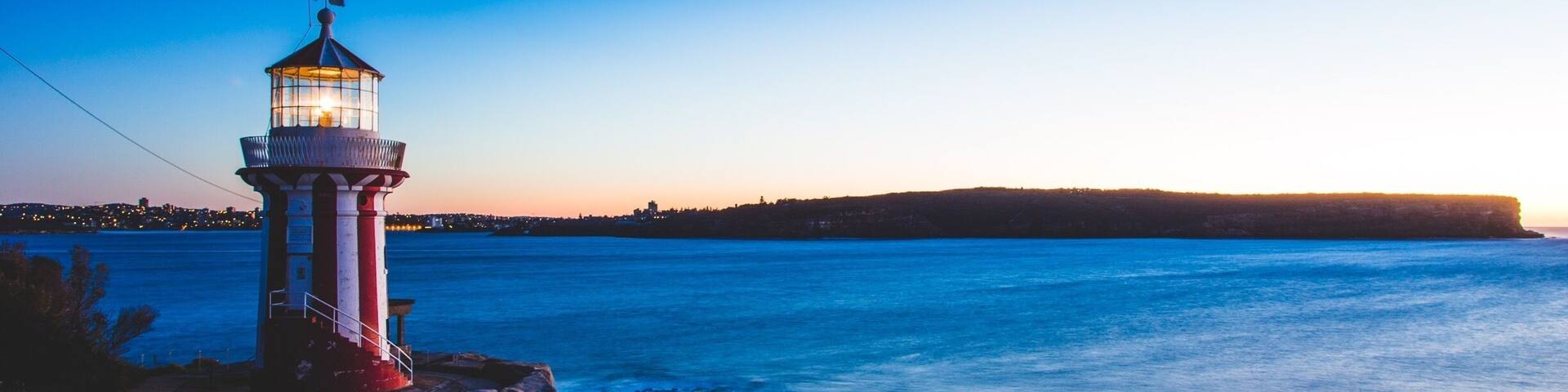 A lighthouse on a rocky shore with a view of the ocean and a distant shoreline at sunset.
