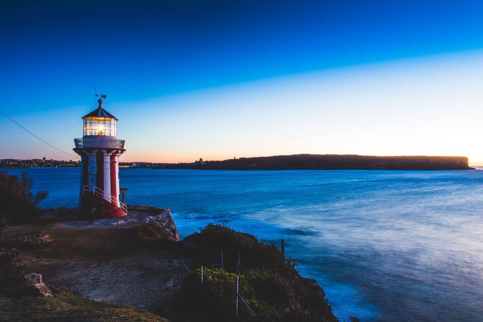 A lighthouse on a rocky shore with a view of the ocean and a distant shoreline at sunset.