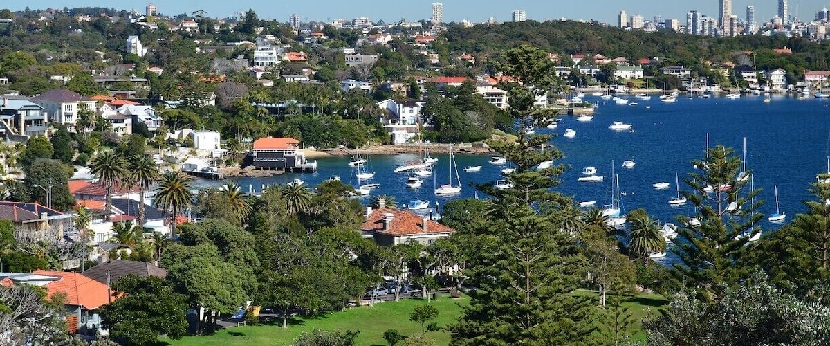 A coastal cityscape with a marina filled with boats, surrounded by residential buildings and greenery.