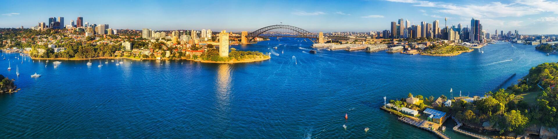 A coastal cityscape with a prominent bridge, high-rise buildings, and a marina with boats.