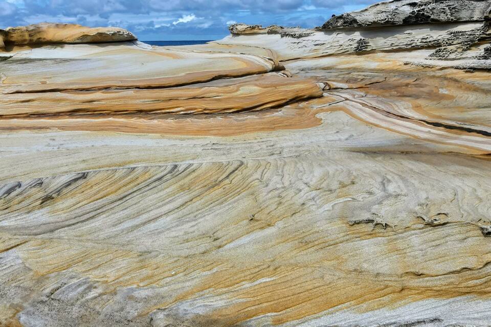 A geological formation with layered rock patterns near a coastal area.
