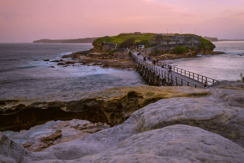 A coastal scene with a pier leading to a grassy island with buildings.