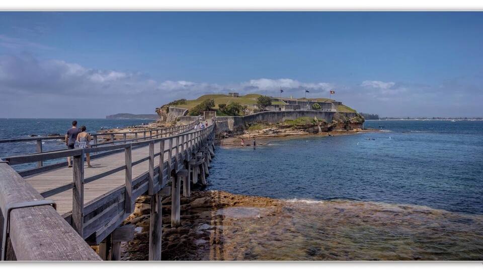 A coastal fortification with a wooden pier extending into the sea, surrounded by rocky terrain and clear skies.