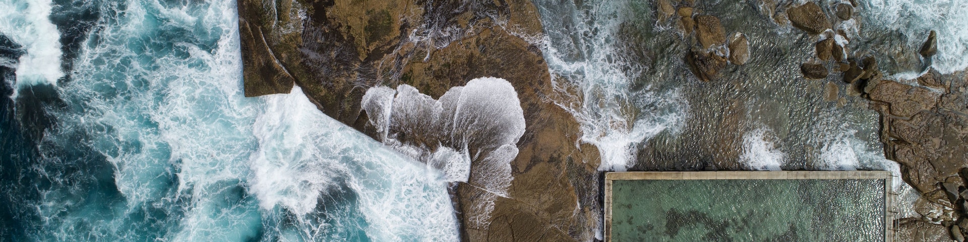 A rocky coastline with turbulent waves and a man-made structure.