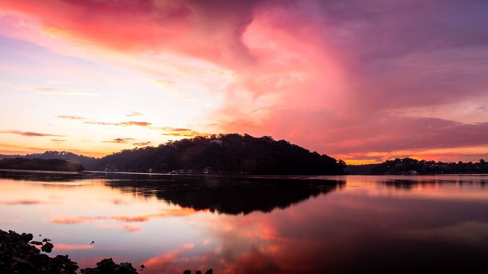 Um lago tranquilo refletindo um pôr do sol com tons de rosa e roxo no céu.