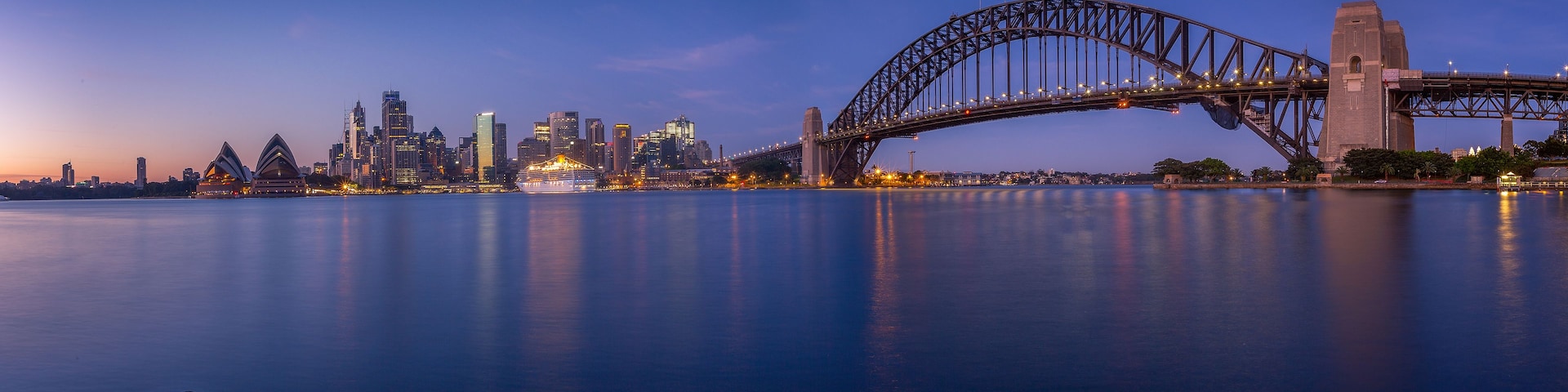 A Ponte Sydney ao entardecer, com a Ópera de Sydney e o horizonte da cidade ao fundo.