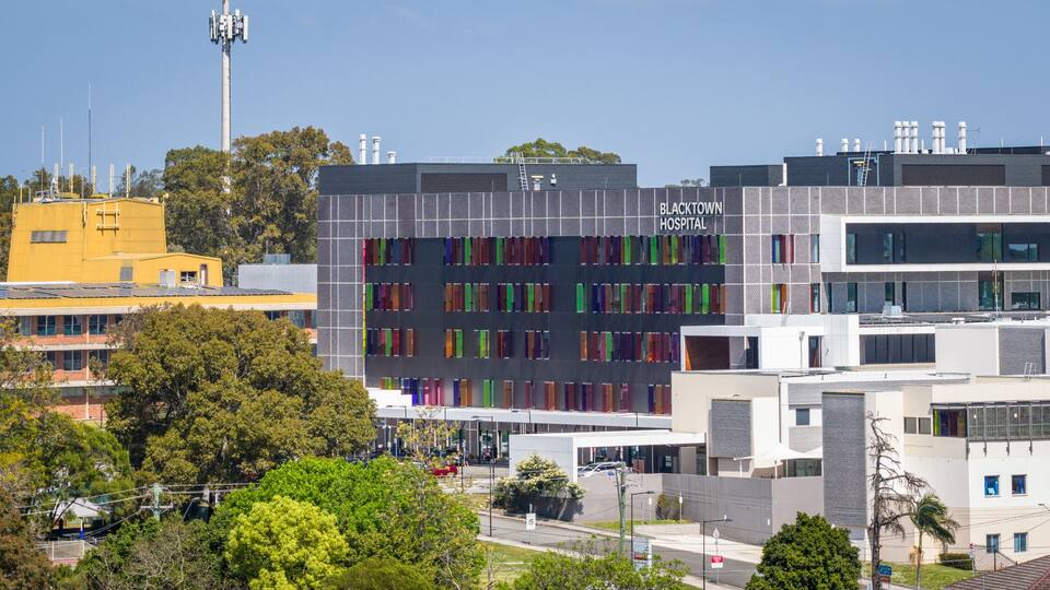 A modern hospital building with colorful window patterns, surrounded by urban infrastructure and greenery.