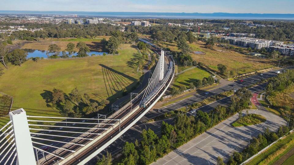 A cable-stayed bridge with a train on it, surrounded by green fields and buildings.