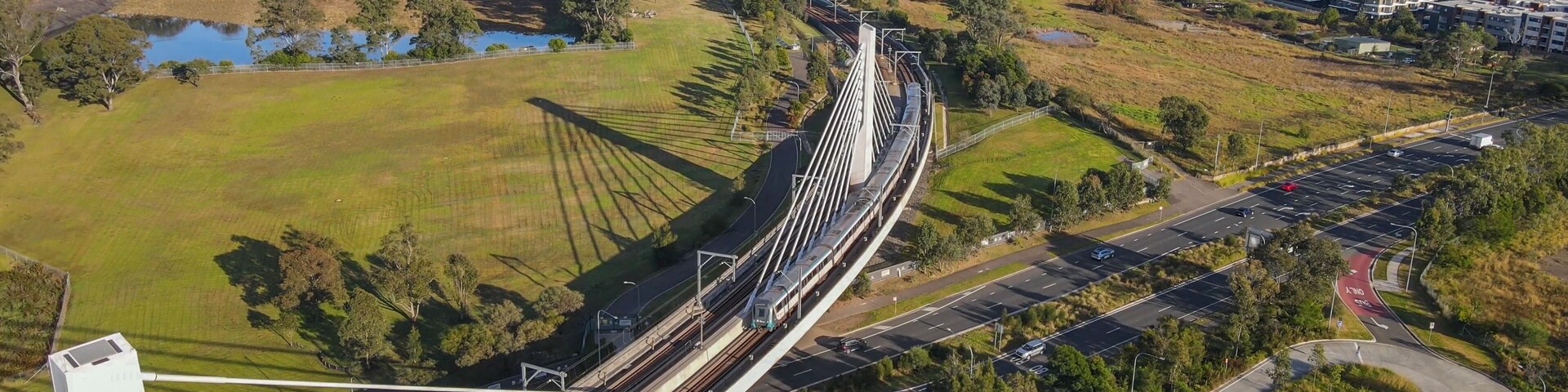 Aerial drone view of a train crossing the railway bridge as it travels toward Rouse Hill Station on the metro northwest railway line, Greater Sydney, NSW Australia in June 2024