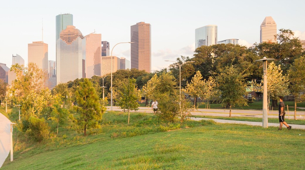 Panorama of downtown Houston, Texas, USA at sunset from Eleanor Tinsley Park. Grassy green park lawn, Buffalo Bayou river, curved pathway with people walking, biking, exercising and modern skylines.