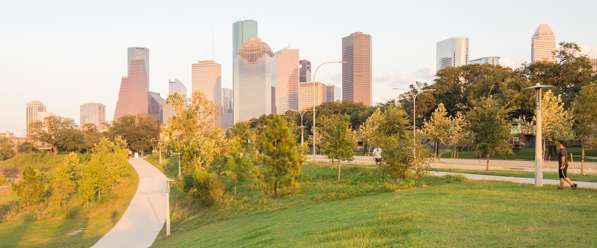 Panorama of downtown Houston, Texas, USA at sunset from Eleanor Tinsley Park. Grassy green park lawn, Buffalo Bayou river, curved pathway with people walking, biking, exercising and modern skylines.