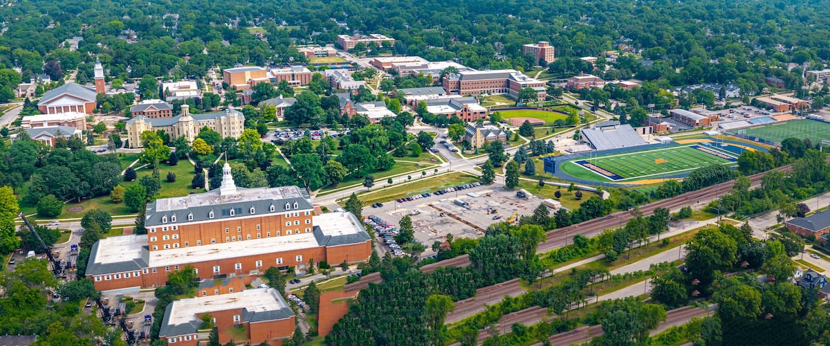 An aerial view of a university campus with multiple buildings, a football field, and surrounding greenery.