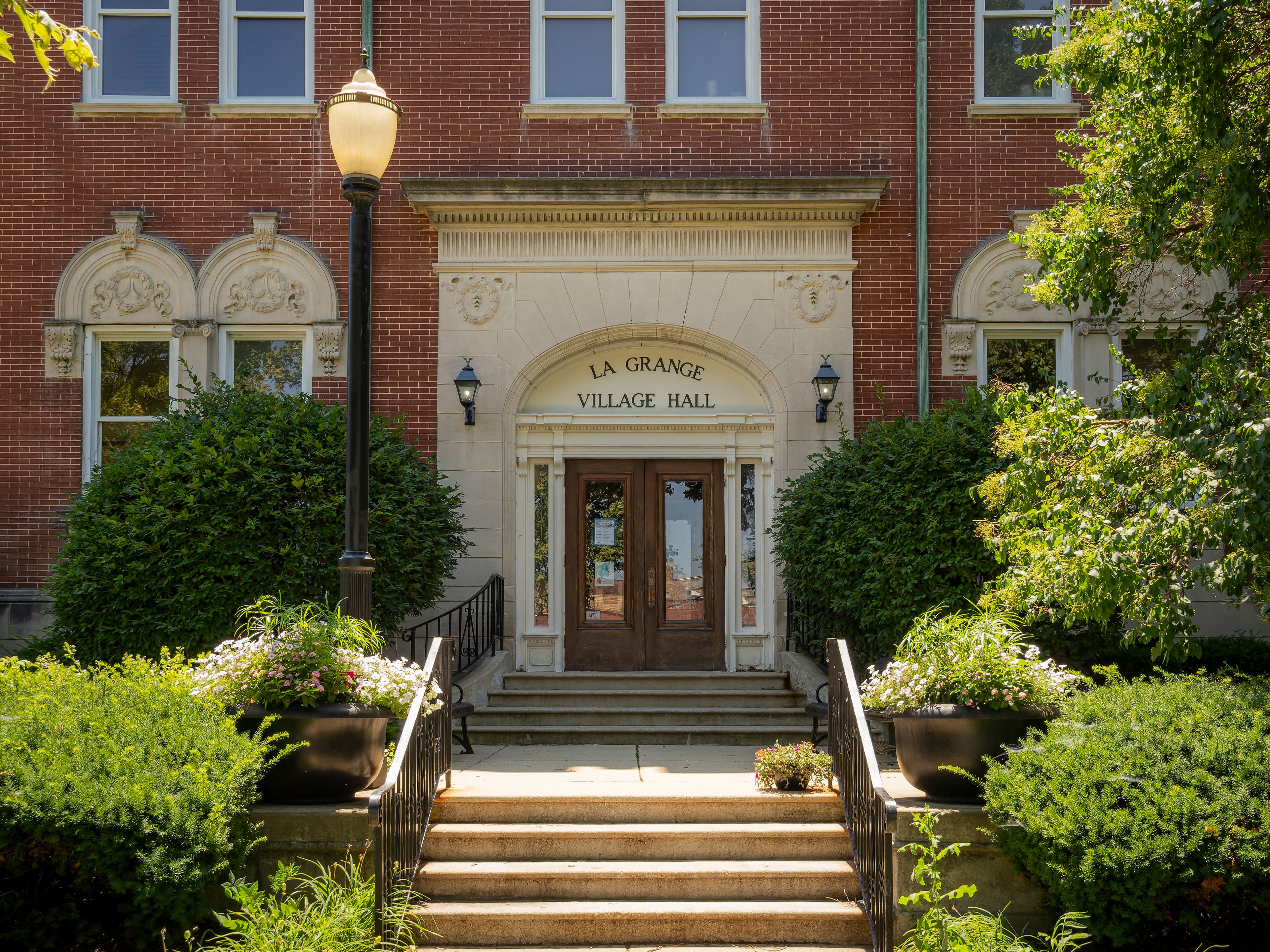 Historic red brick facade and arched entrance of the La Grange Village Hall municipal building on a sunny day with green landscaping and steps