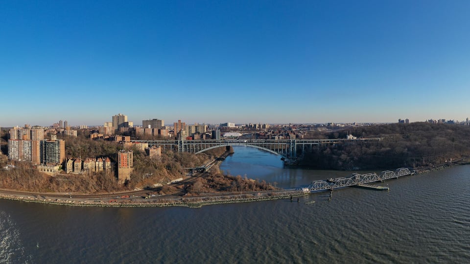 A river with a bridge, a city skyline, and a forested area.