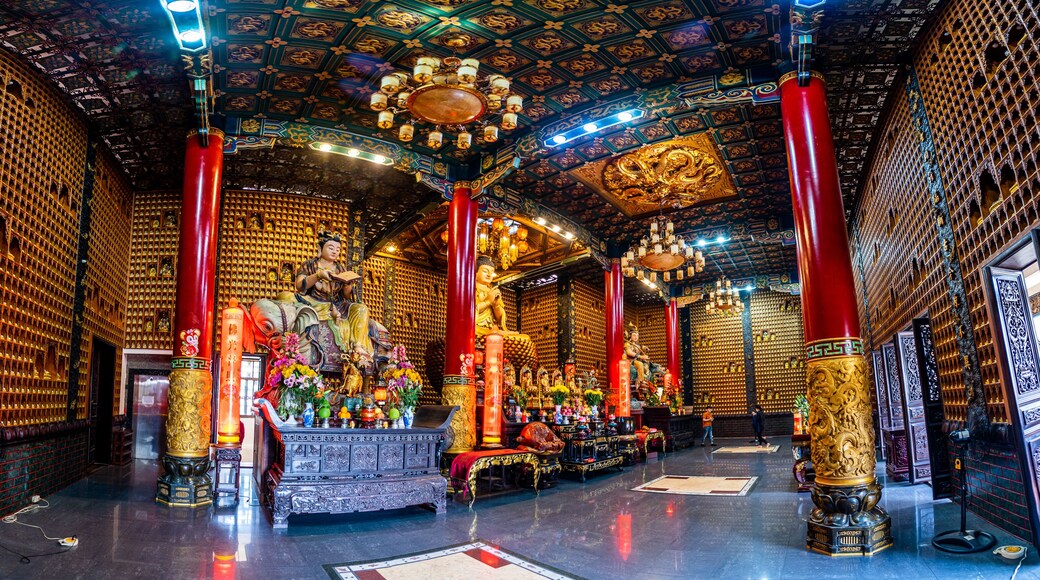 A temple interior with ornate decorations, golden statues, and red pillars.