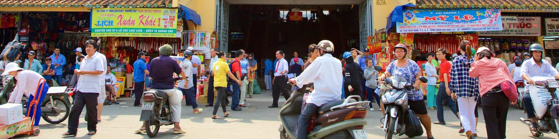 A busy street with a traditional building entrance, colorful flags, and various shops.