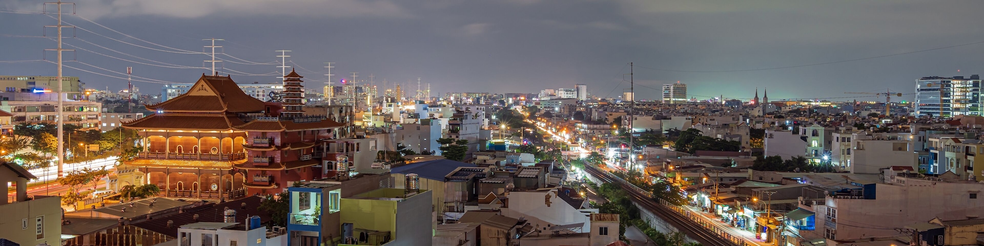 A cityscape at night with illuminated buildings, a prominent pagoda, and a busy railway track.