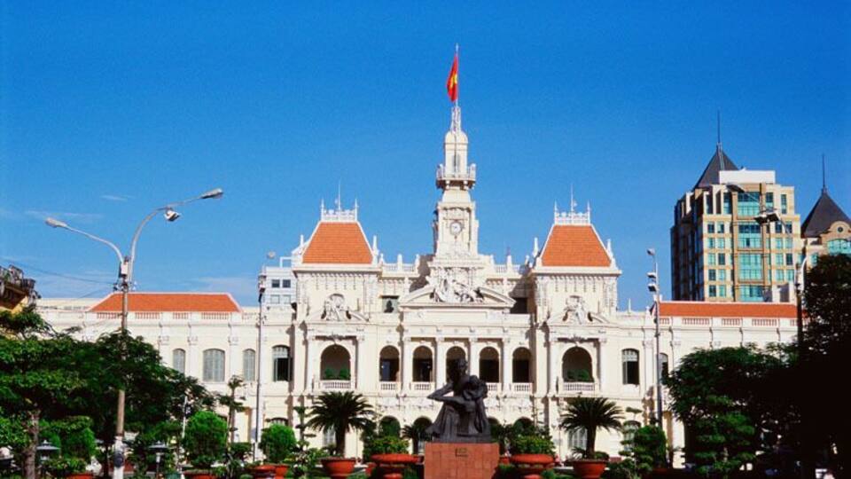 A grand building with a central statue, surrounded by well-maintained gardens and palm trees.