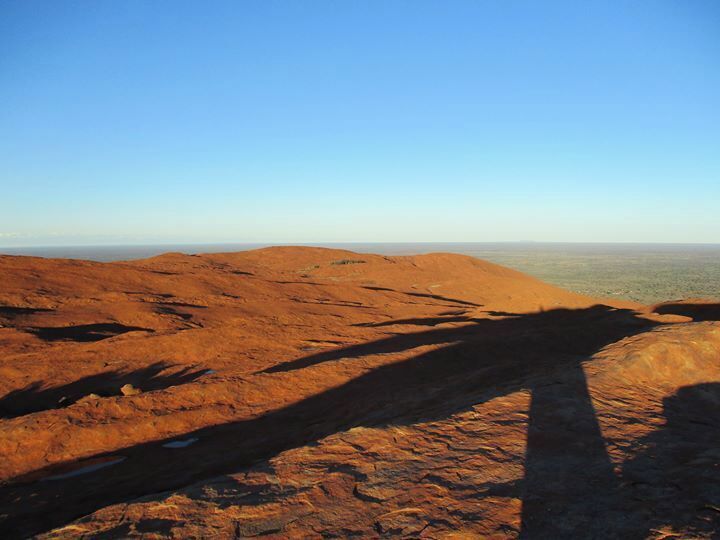A vast, reddish-brown desert landscape with rolling hills and a clear blue sky.