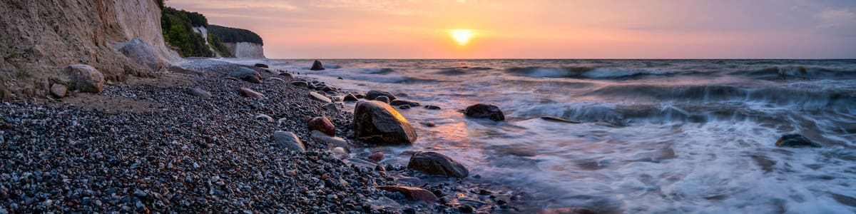 A rocky beach with a cliff, ocean waves, and a sunset.