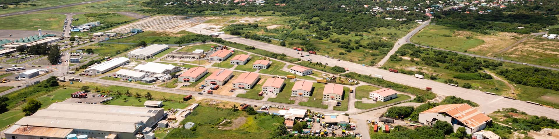 An aerial view of a coastal industrial area with warehouses, roads, and a distant view of the ocean.