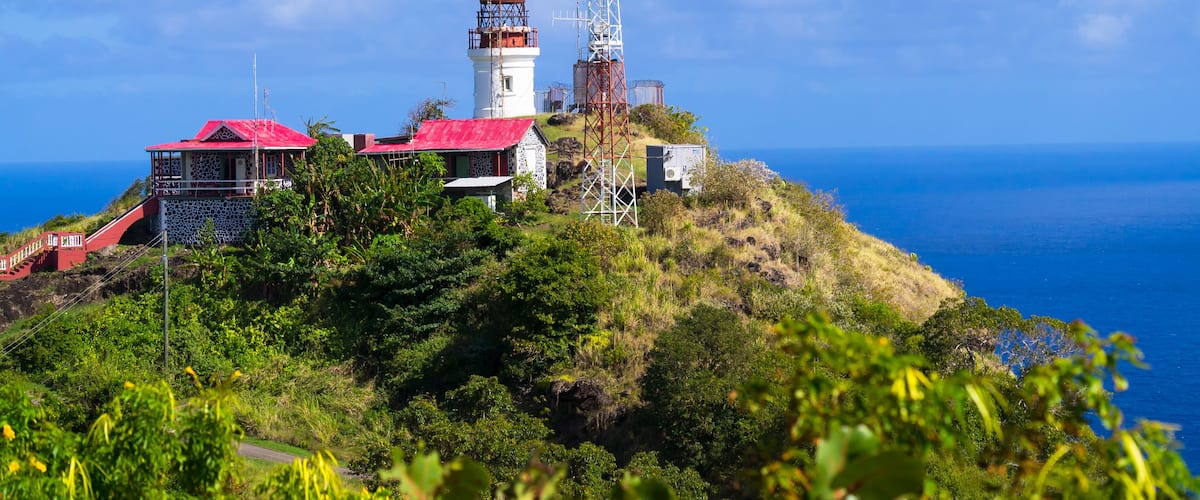 A coastal landscape with a lighthouse, a red-roofed building, and a communication tower.