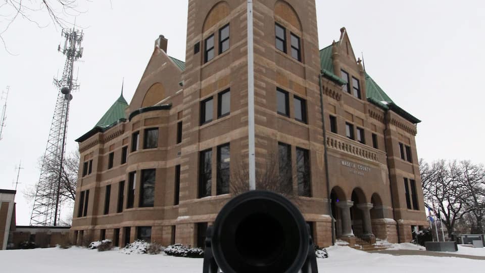 A historic building with a clock tower, an American flag, and a cannon in the foreground.
