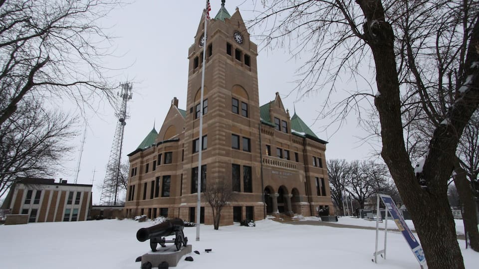 A historic building with a clock tower, surrounded by snow-covered ground and leafless trees.