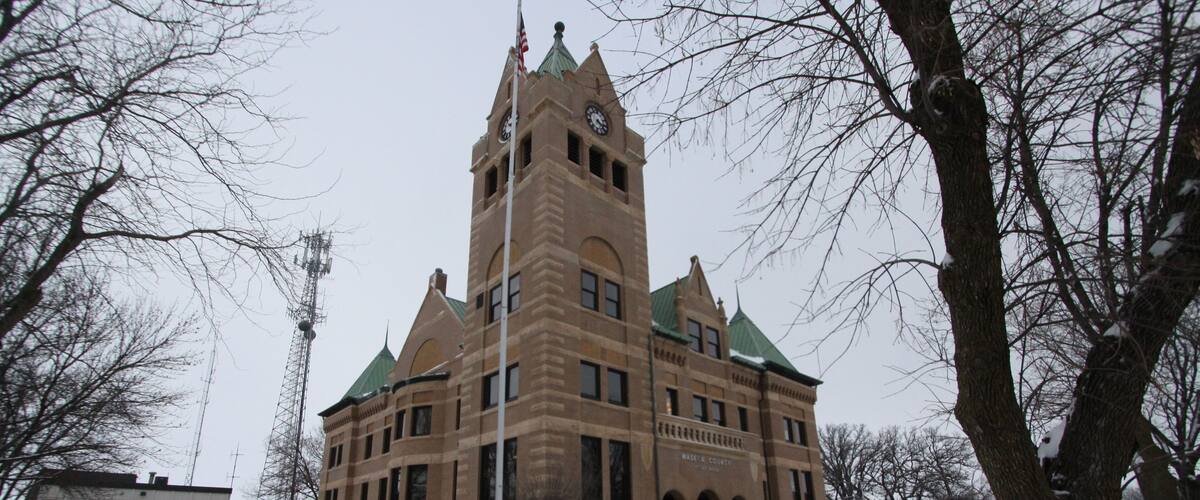 A historic building with a clock tower, surrounded by snow-covered ground and leafless trees.