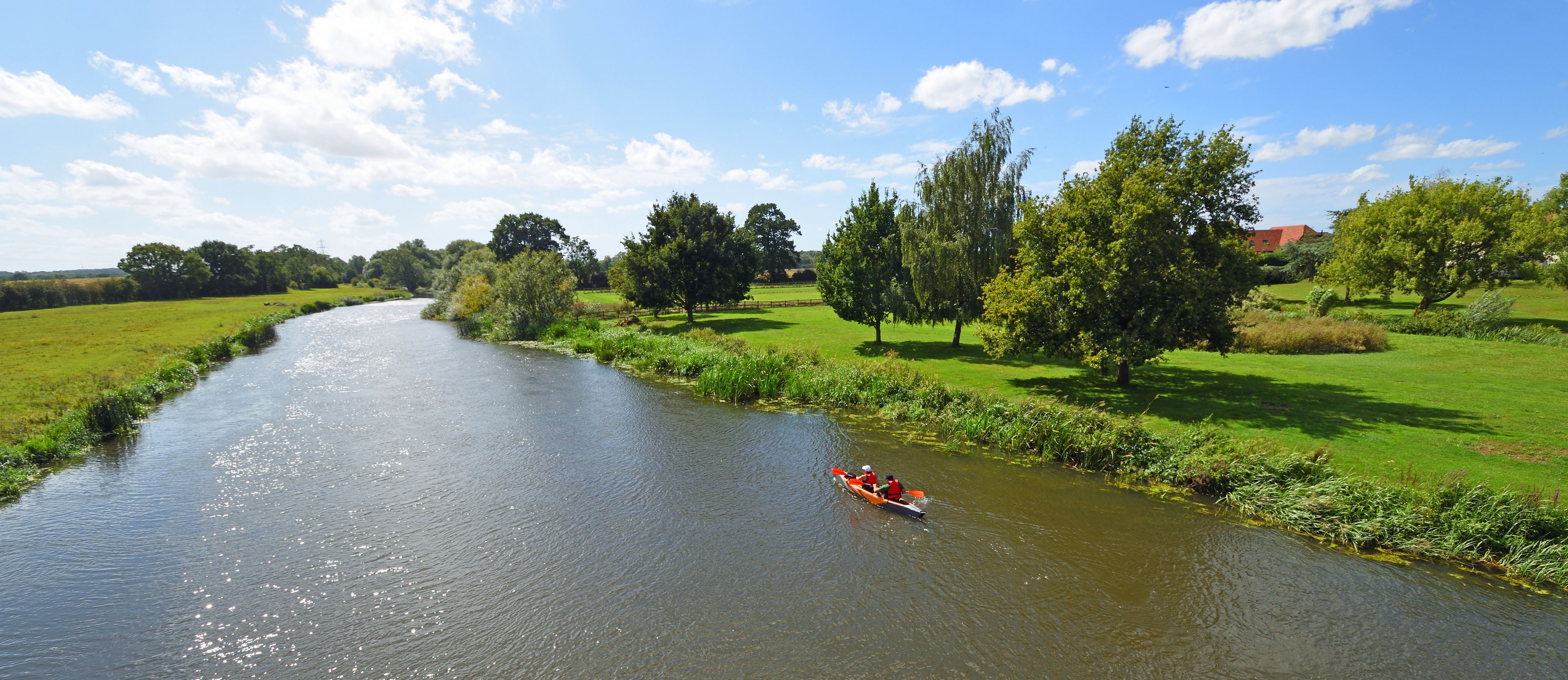 A river with a narrowboat on it, surrounded by green fields and trees.