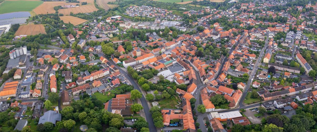 An aerial view of a town with red-roofed buildings, green spaces, and a church spire.