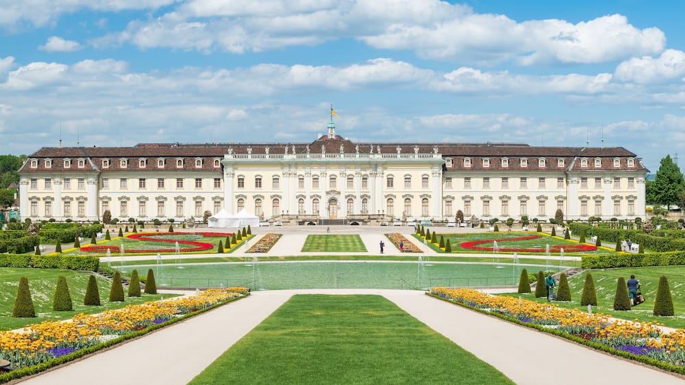Ein großes, historisches Gebäude mit symmetrischen Gärten und gepflegten Rasenflächen.