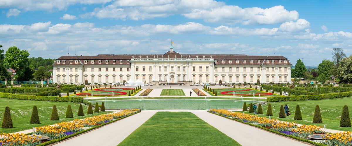 A large, historic building with symmetrical gardens and manicured lawns.