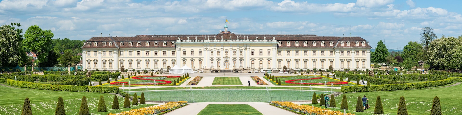 A large, historic building with symmetrical gardens and manicured lawns.